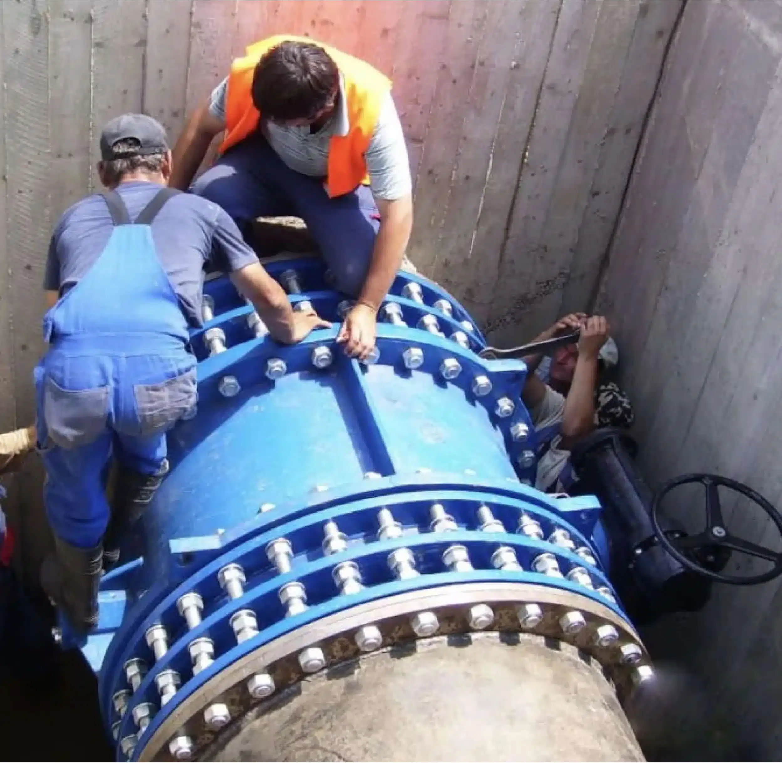 Workers struggling to remove a large valve from a pipeline