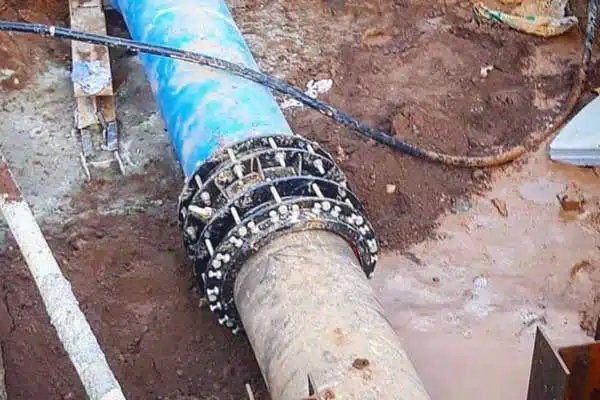 A flexible coupling connecting an old cast iron pipe to a new PVC pipe in a trench