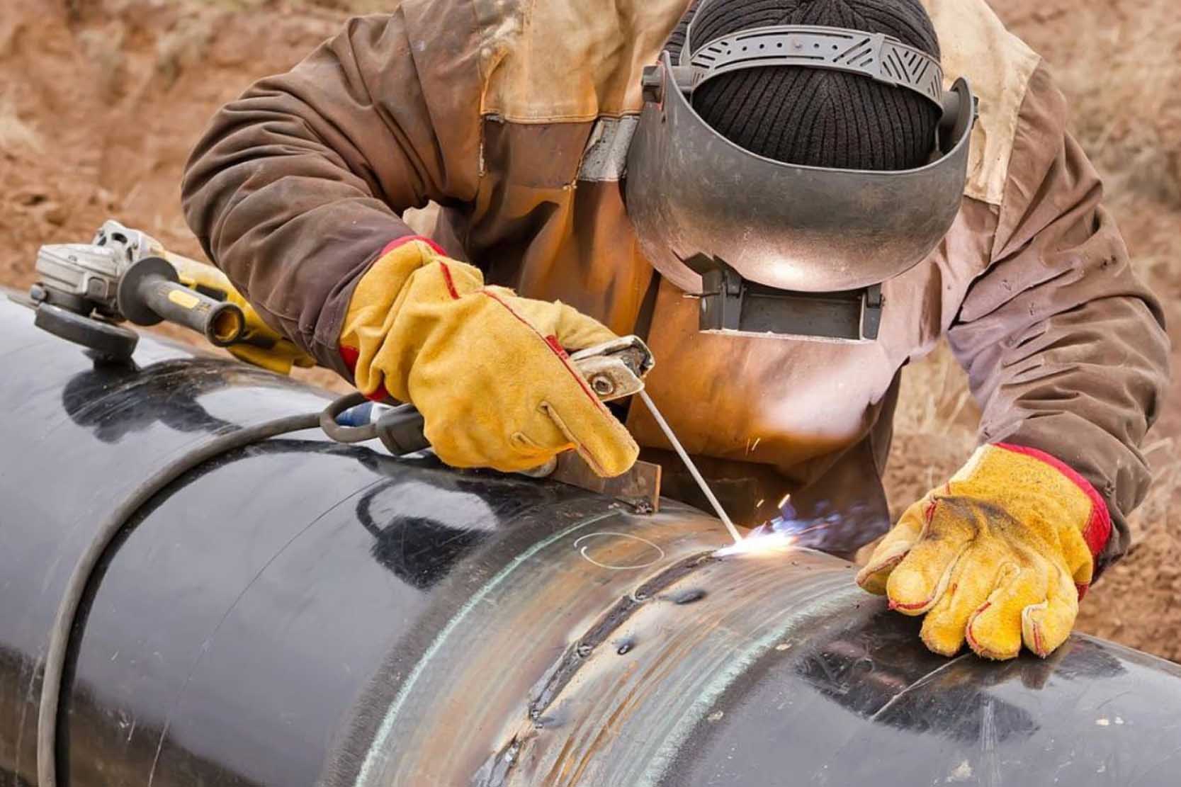 Welder working on a large industrial pipe section in a controlled environment